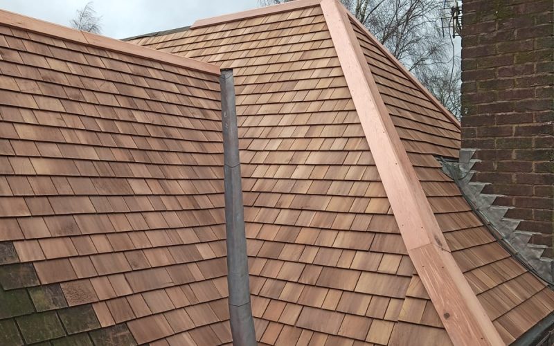 A brown shingled roof with a chimney, featuring new wooden slates being installed